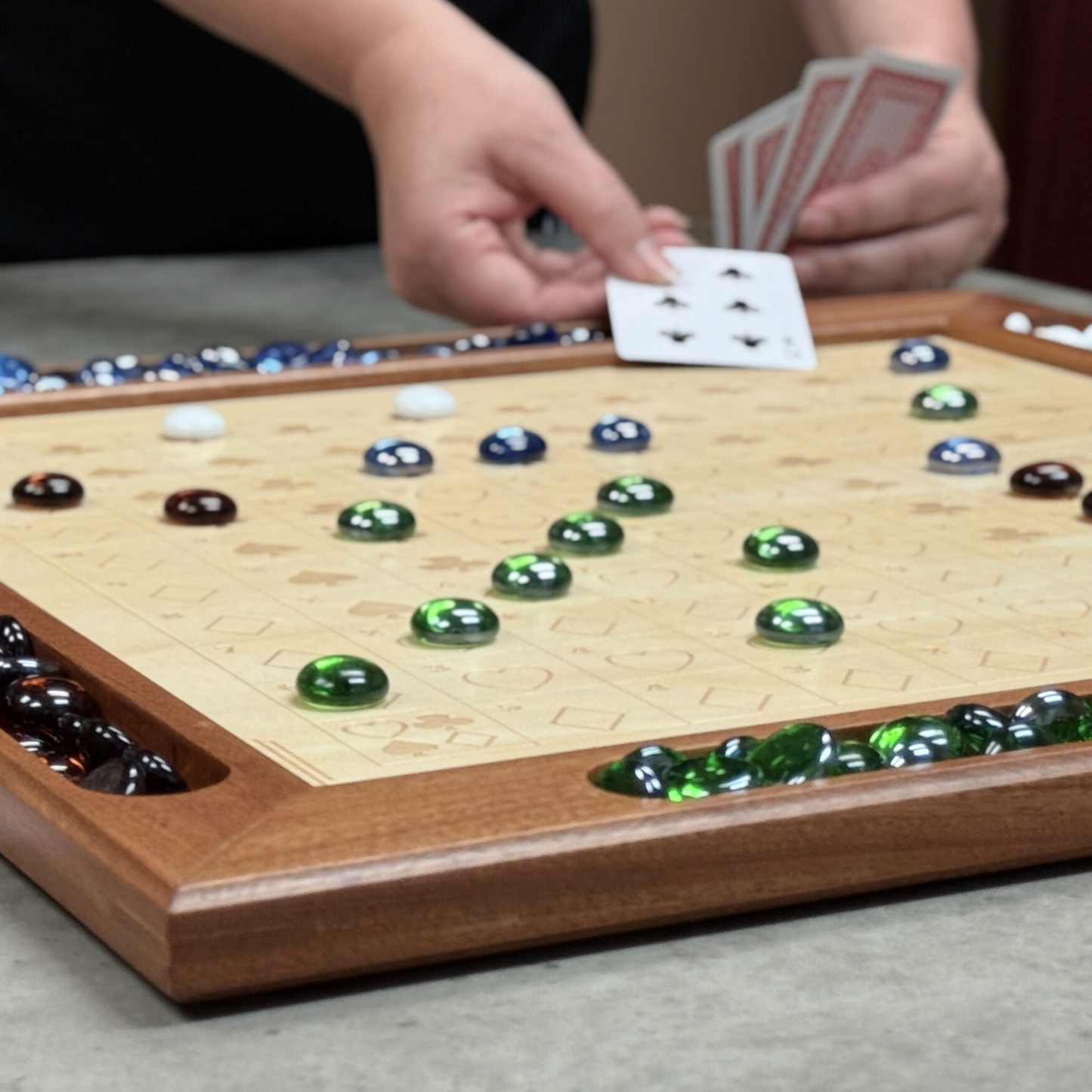 Board game with wooden frame and green and black stones, being played with cards.