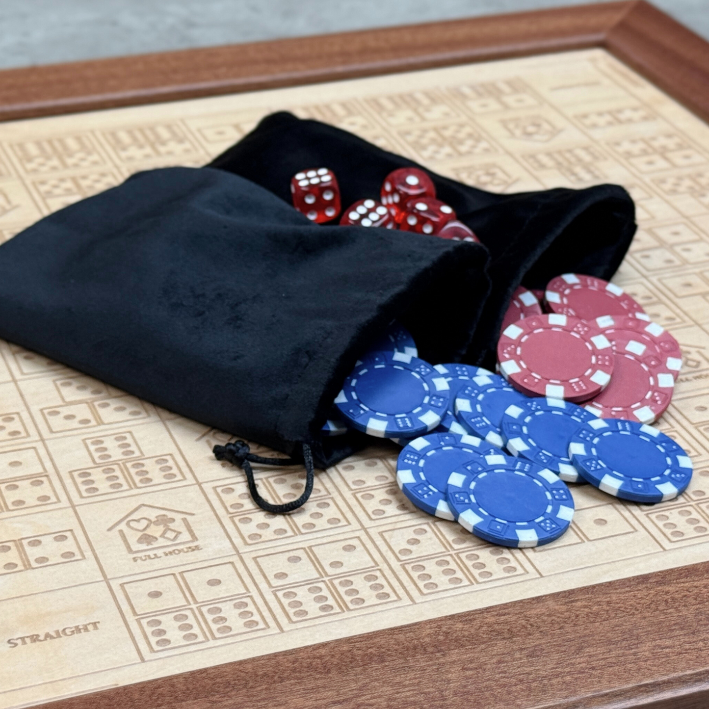 Black drawstring bag with red and blue poker chips and dice on a wooden surface.